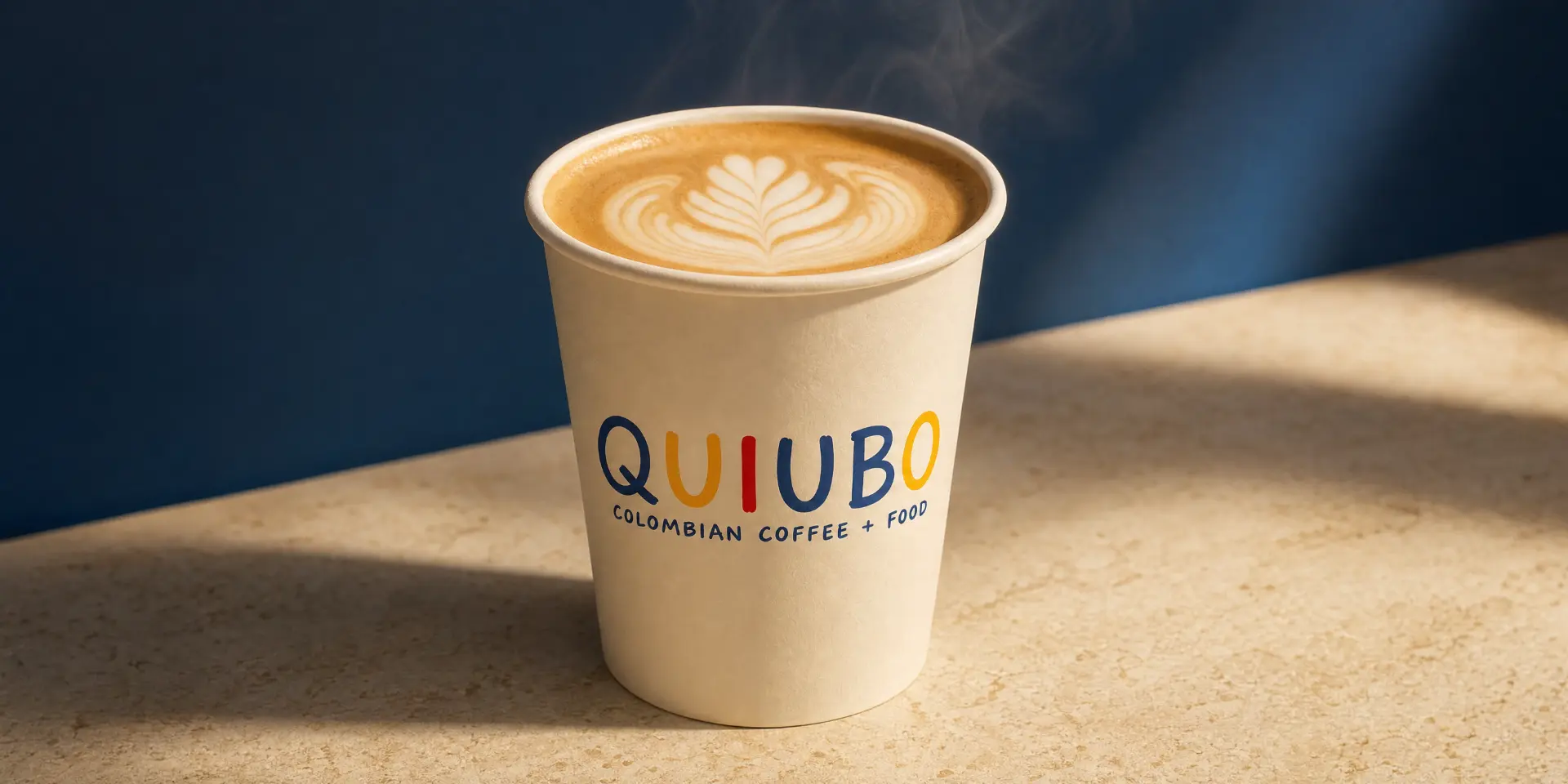 Latte QUIUBO en vaso de papel crema con arte latte en roseta frente a una pared azul