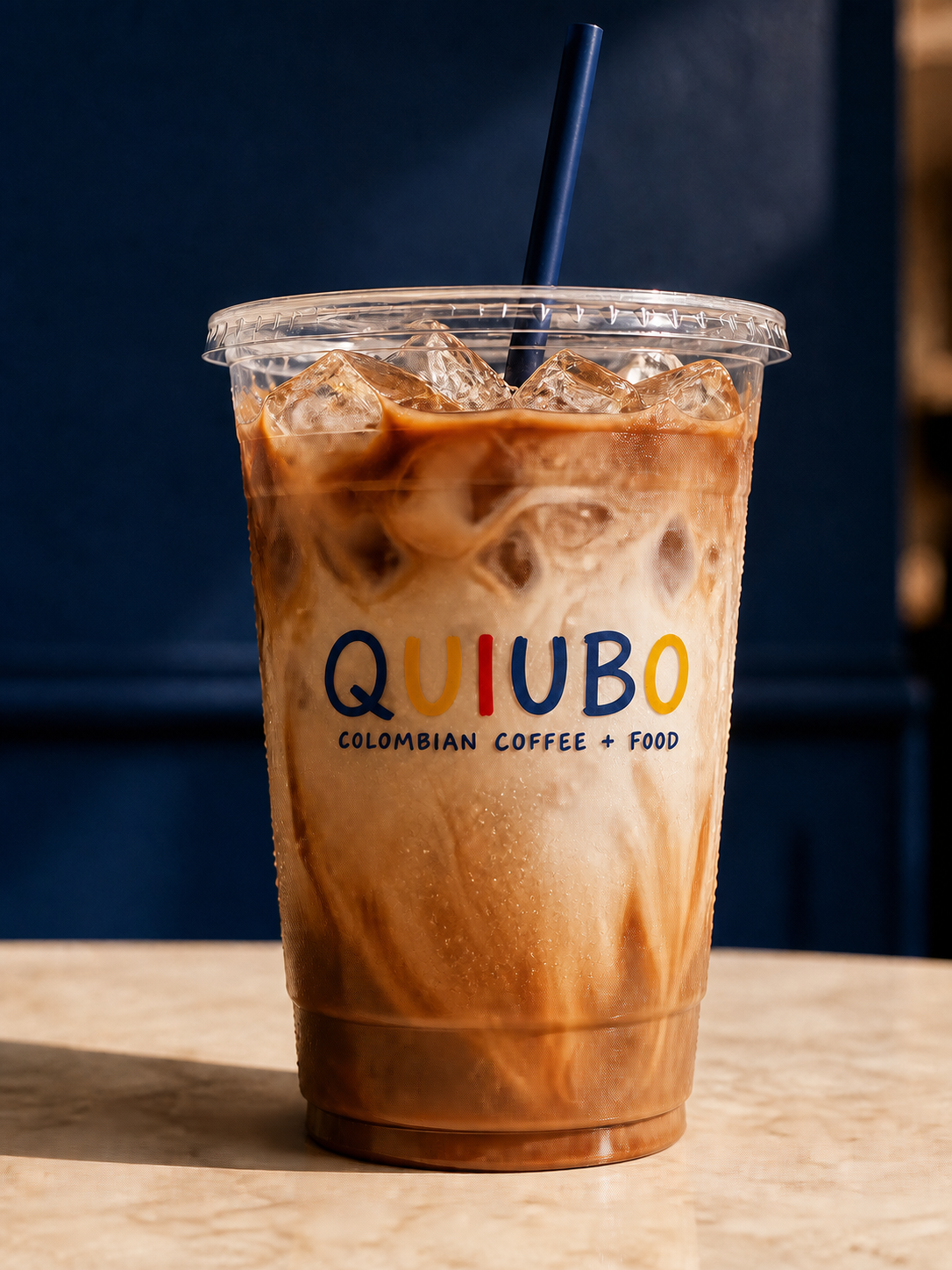 Mocha fría QUIUBO en vaso transparente con hielo, remolinos de leche y pitillo azul
